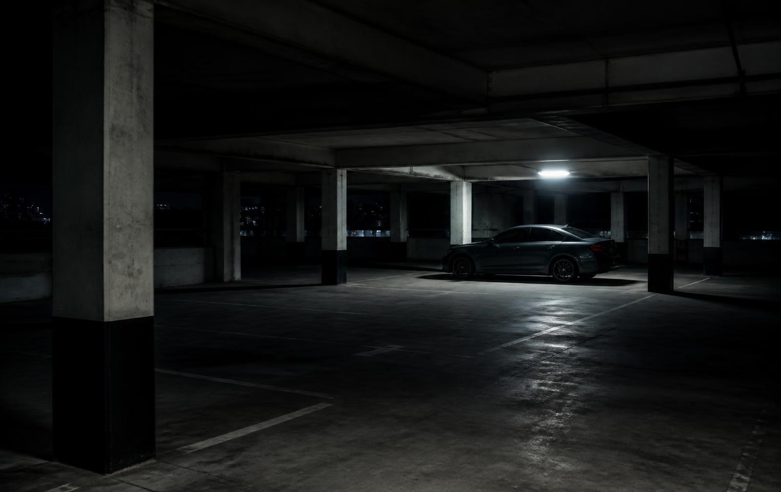 Single car parked under a light in a dark concrete parking garage